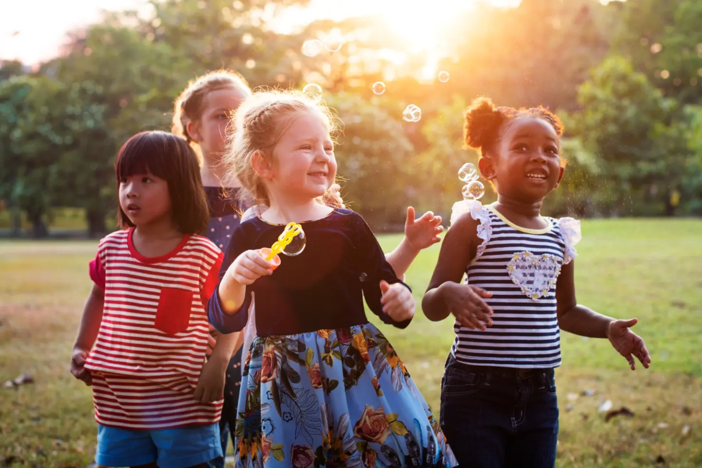 Fyra skrattande barn leker utomhus i en grön park i solnedgången