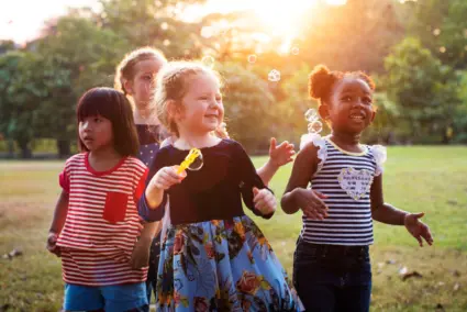 Fyra skrattande barn leker utomhus i en grön park i solnedgången