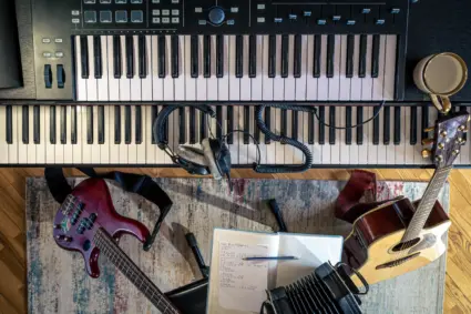 En bild tagen ovanifrån på ett keyboard, en elektrisk gitarr, en akustisk gitarr, trådade hörlurar och ett skrivblock.