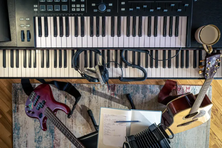 En bild tagen ovanifrån på ett keyboard, en elektrisk gitarr, en akustisk gitarr, trådade hörlurar och ett skrivblock.