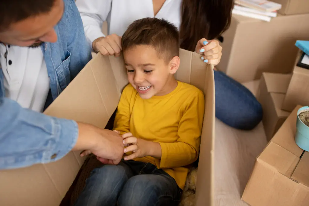 pojke sitter i en låda av kartong, vuxna sträcker sina händer mot pojken för att kittla.