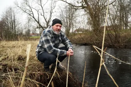Man sitter på huk intill bäck.