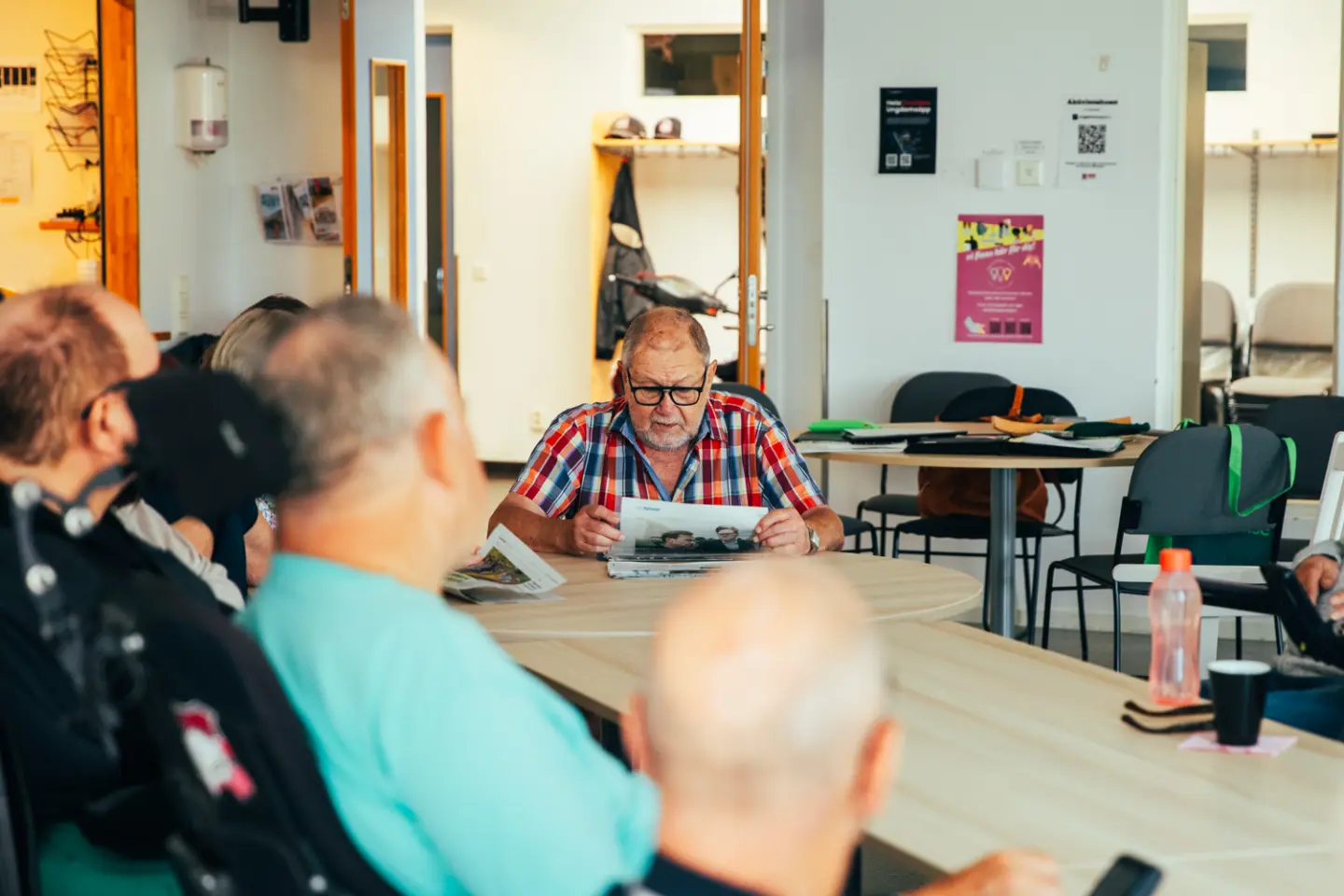 En grupp människor sitter runt ett bord, en man läser ur en tidning