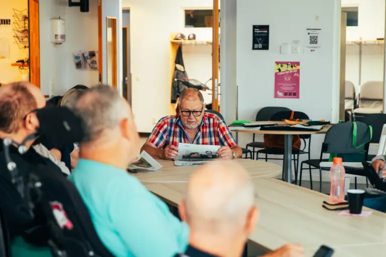 En grupp människor sitter runt ett bord, en man läser ur en tidning
