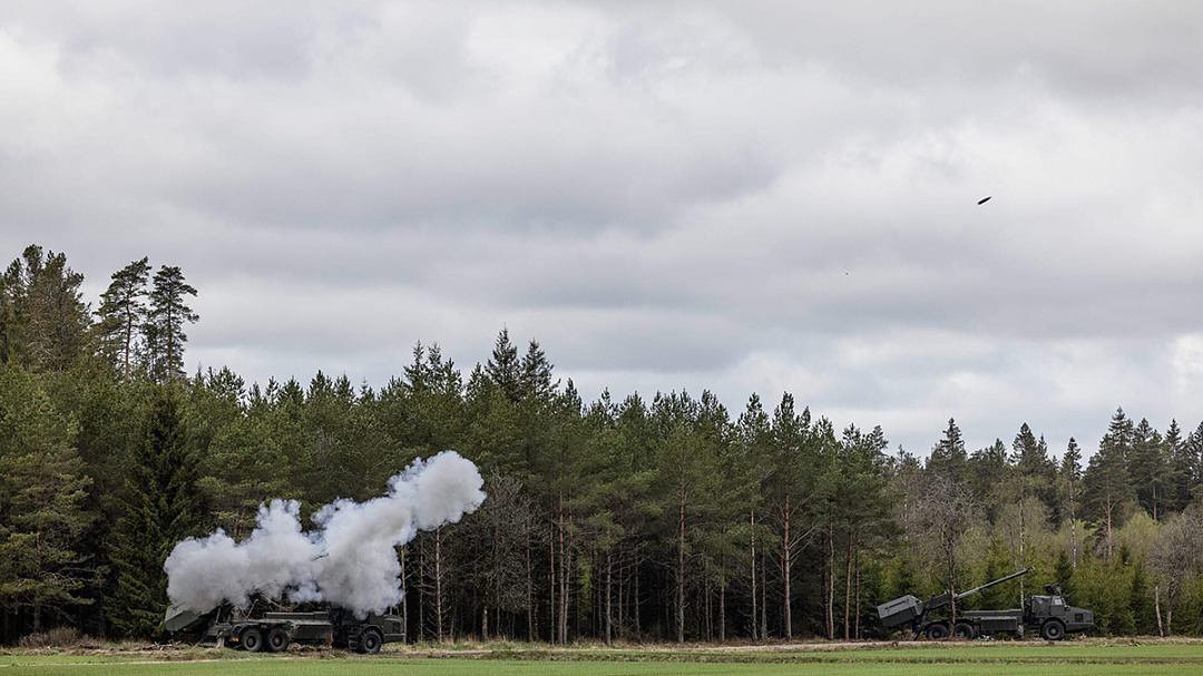 Stridsvagn skjuter på en stor grönyta.