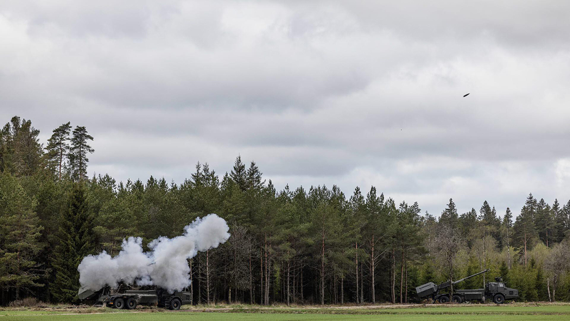 Stridsvagn skjuter på en stor grönyta.