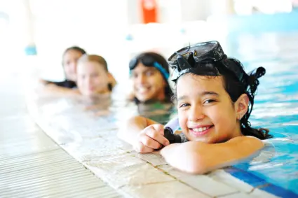 Barn på rad i kanten på en pool tittar upp från vattnet