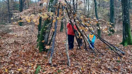 vuxen och barn som bygger koja av pinnar i skogen