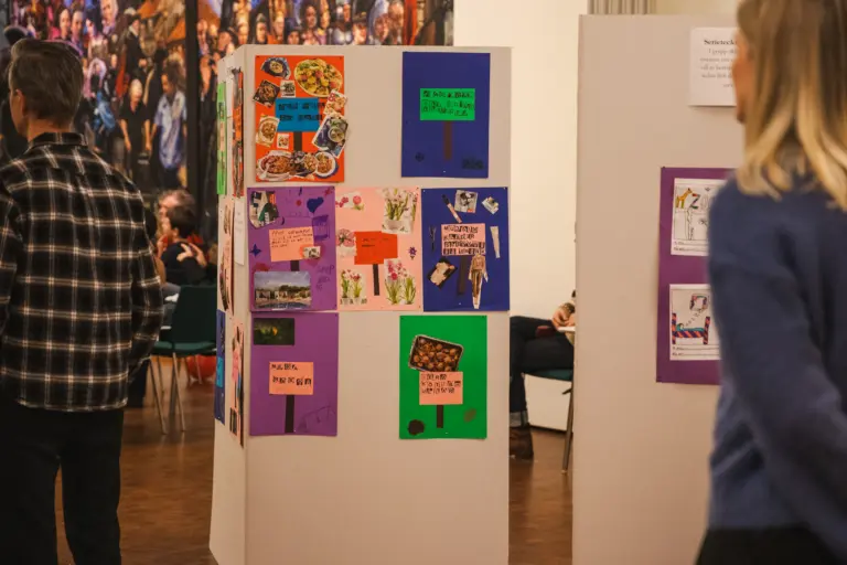 Färgglada teckningar och kollage gjorda av barn är uppsatta på en vikvägg. Folk står runtomkring och kollar på dem