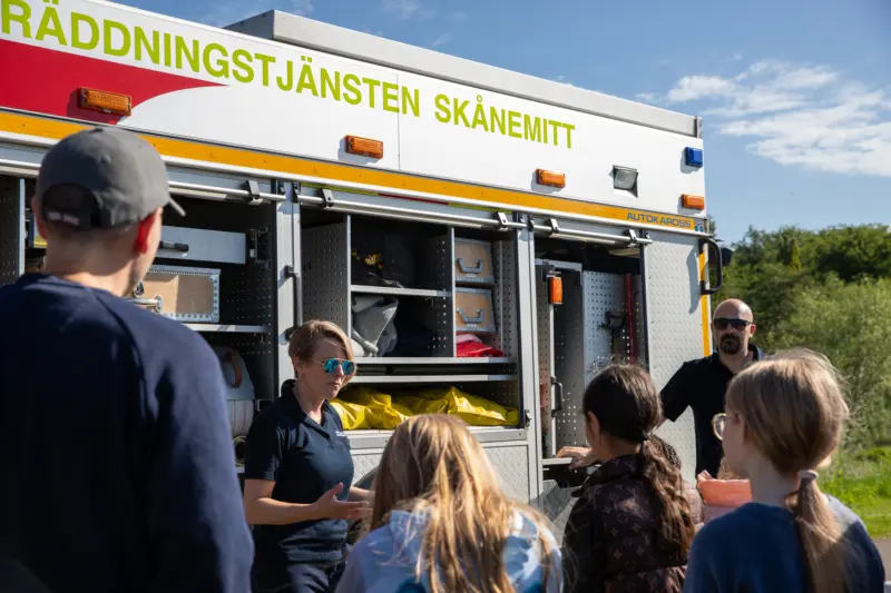 kvinna står vänd med ryggen mot och hjälper ett barn att hålla i en vattenslang.
