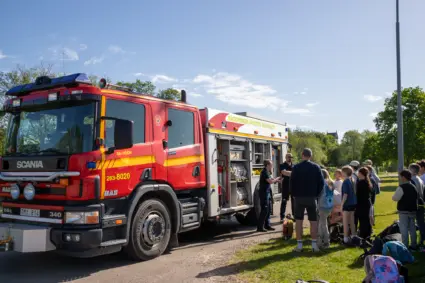 flera barn står och pratar med några vuxna vid en brandbil.