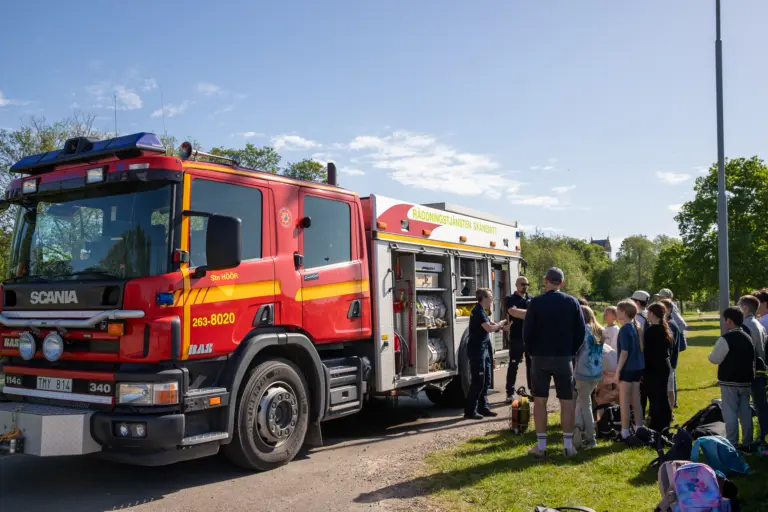 flera barn står och pratar med några vuxna vid en brandbil.