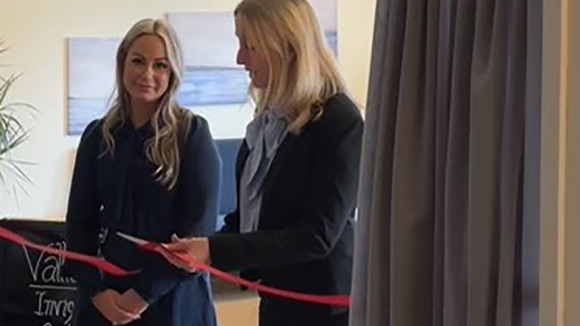 Två kvinnor står vid ett band, den ena klipper bandet med en sax.