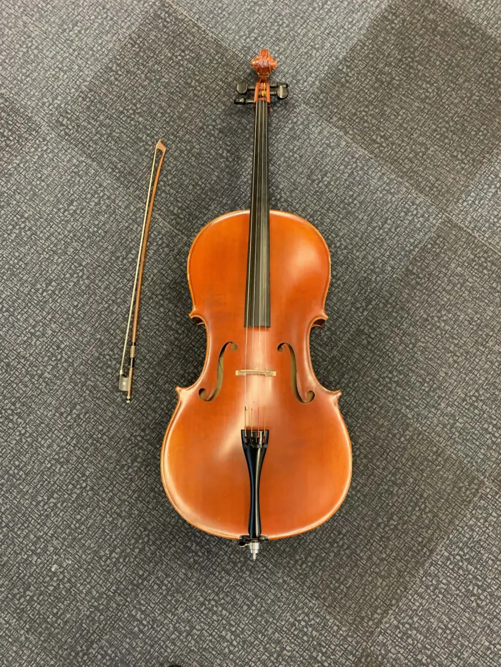 Cello med stråke liggandes på ett grått golv