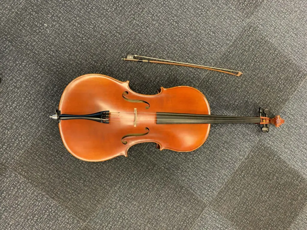 Cello med stråke liggandes på ett grått golv