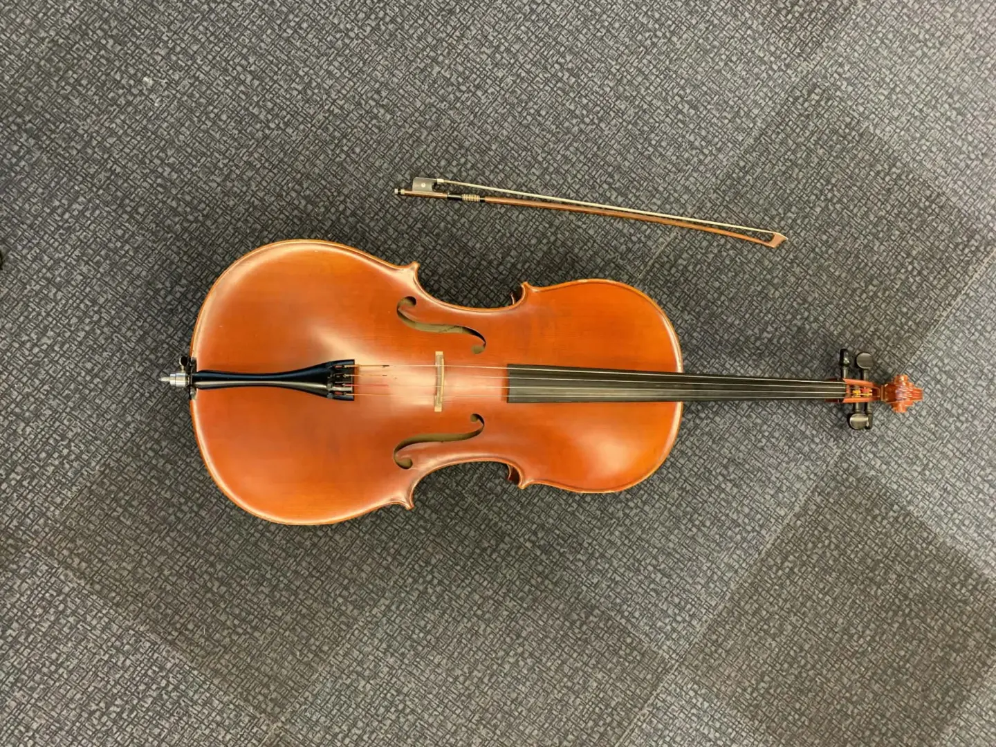 Cello med stråke liggandes på ett grått golv