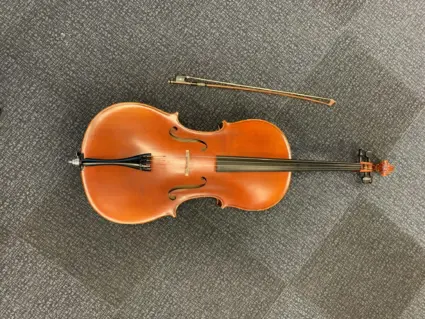 Cello med stråke liggandes på ett grått golv