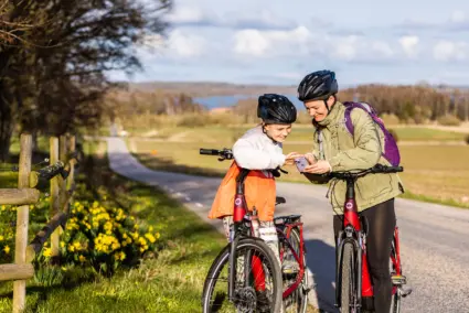 en vuxen och ett barn står iförda cykelhjälmar och tittar i en mobil. Båda gränslar sina cyklar