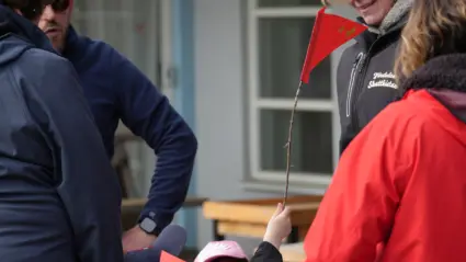 En barnhand viftar med en röd liten flagga framför vuxna