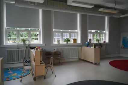Förskolerum med stolar, hyllor och leksaker.
