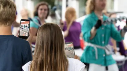 Två barn filmer ett framtränade med sina mobiltelefoner. I bakgrunden syns personer som dansar och spelar trummor.