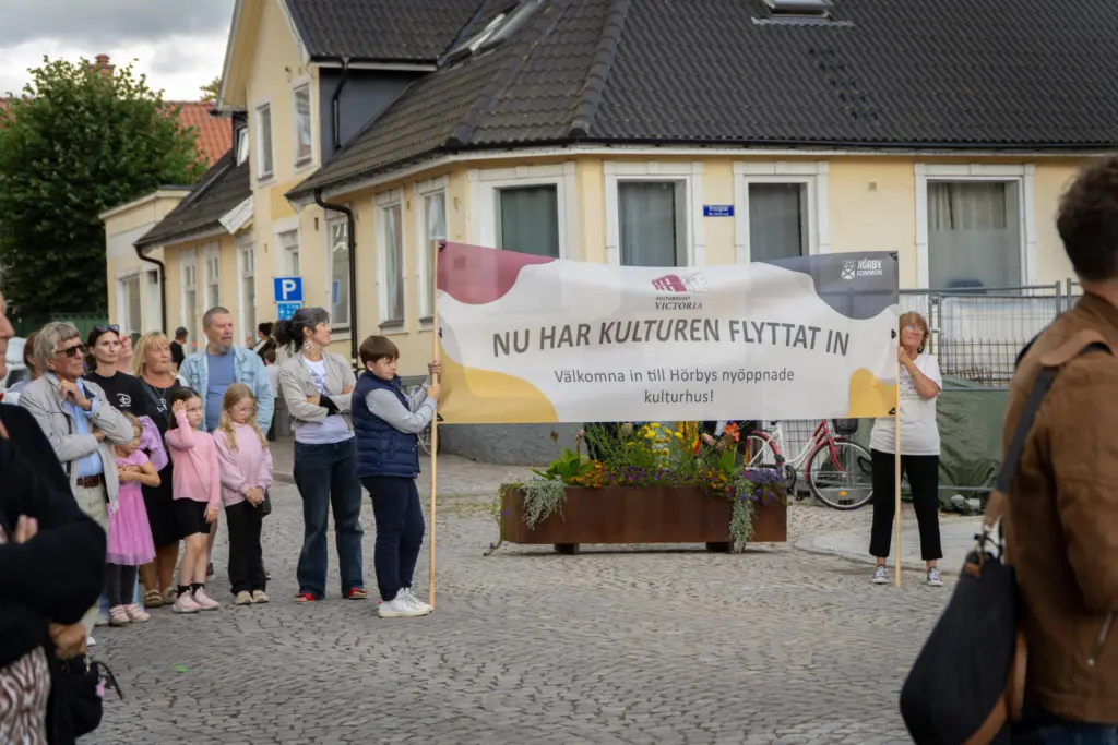 Bild tagen utomhus på en samling människor. Två av dem håller i en stor banderoll med Hörby kommuns logga där det stå "Nu har kulturen flyttat in!"