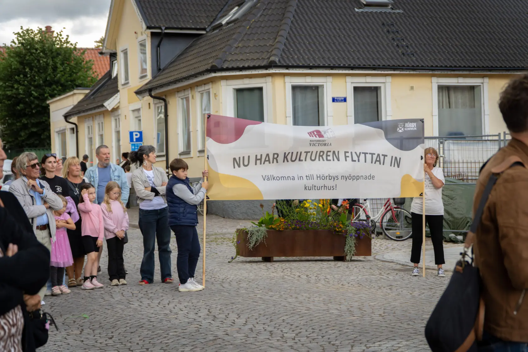 Bild tagen utomhus på en samling människor. Två av dem håller i en stor banderoll med Hörby kommuns logga där det stå "Nu har kulturen flyttat in!"