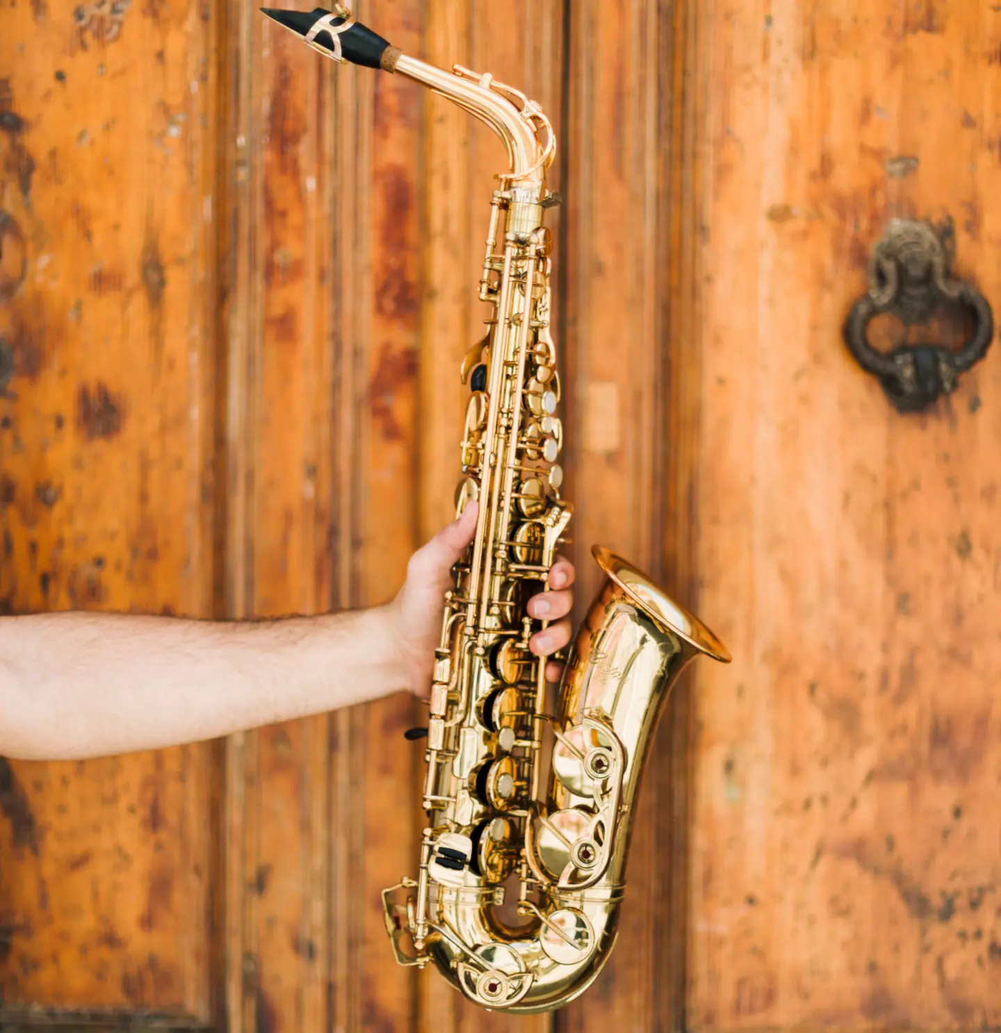 hand håller ut en saxofon framför en bakgrund av trä