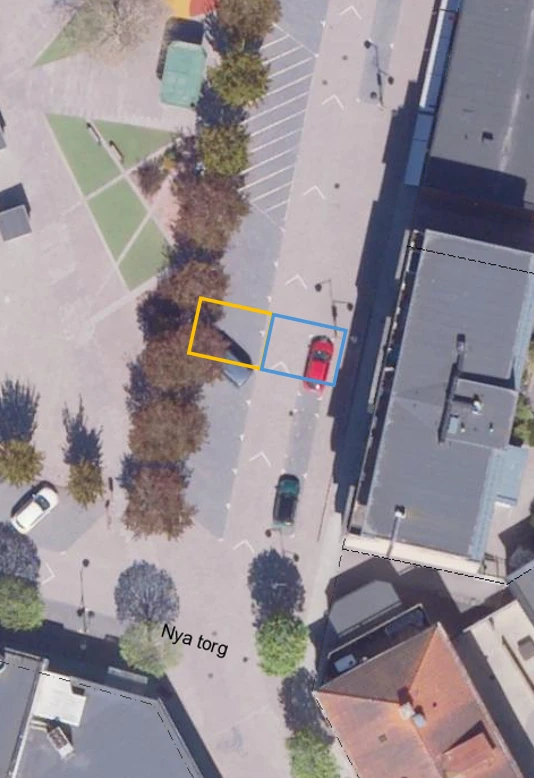 satellitbild p&aring; Nya torg med aktuellt omr&aring;de markerat i gul (bit av parkeringsplats) och bl&aring; (k&ouml;rf&auml;lt invid byggnad)
