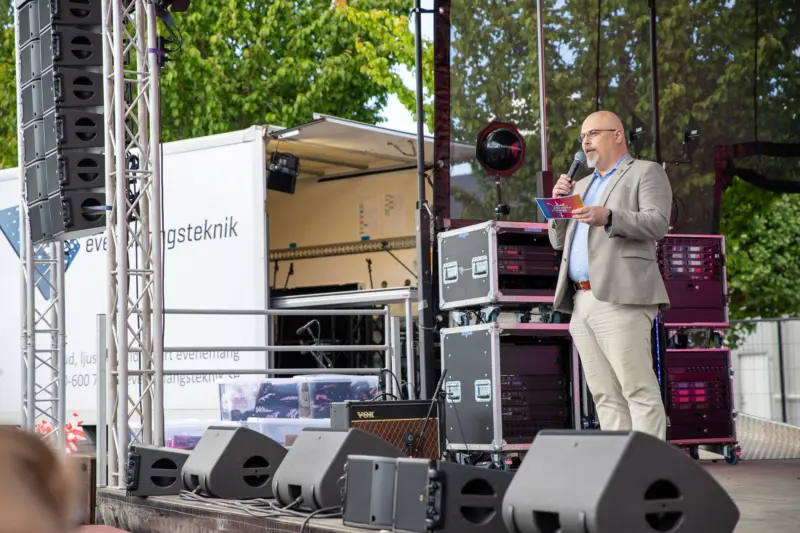 En man st&aring;r p&aring; en utomhusscen och pratar in i en mikrofon.