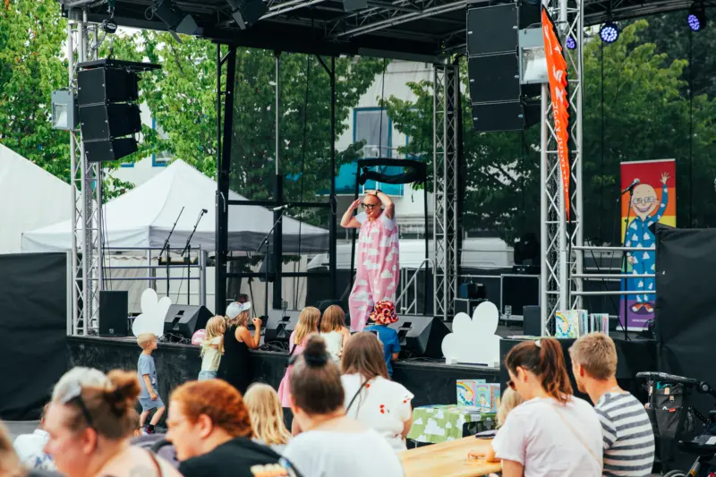 En rosaklädd kvinna står på scen och är i full gång med att sjunga och dansa framför publiken som består av små barn.
