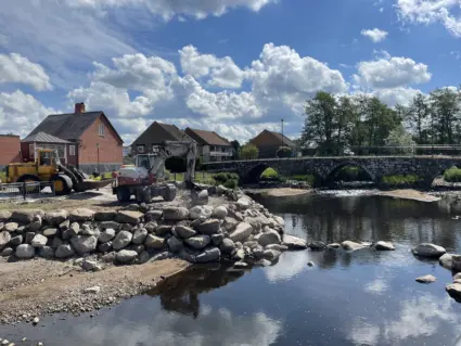 traktoch och grävmaskin på ett en byggplats vid ett vattendrag