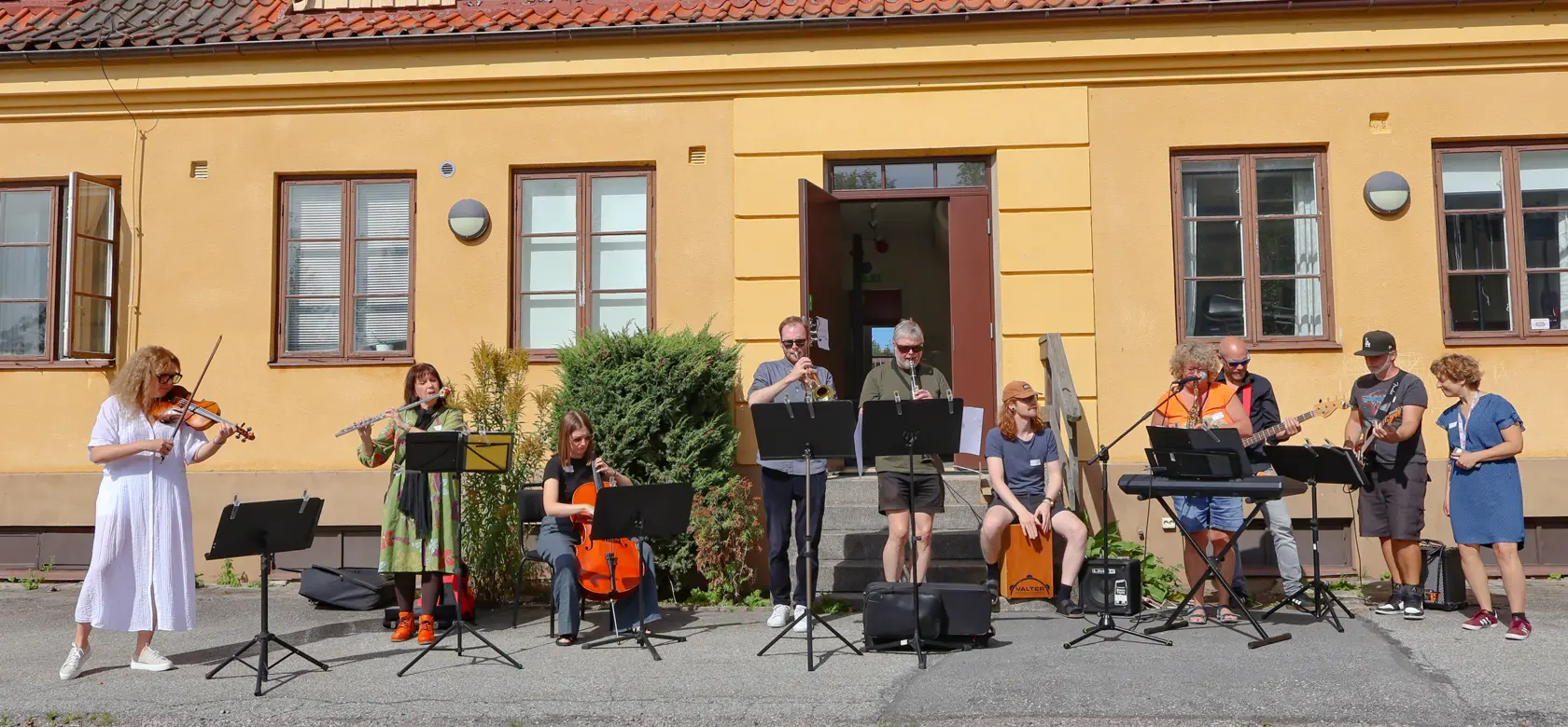 Hörby kulturskola, lärare med instrument poserar framför en gul byggnad