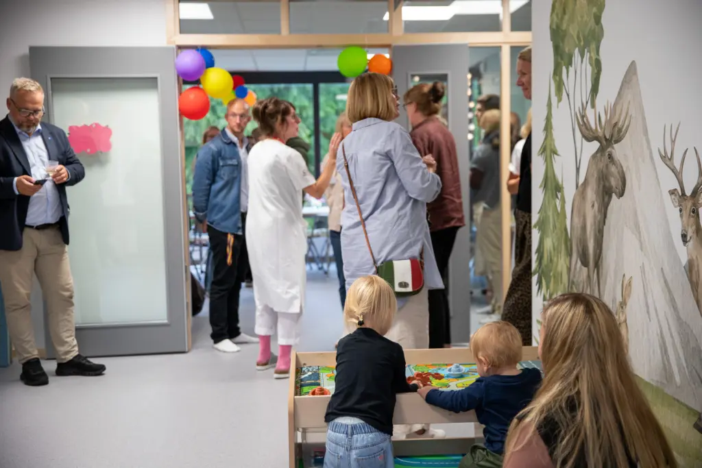 Många människor samlade i en lokal. Små barn leker med leksaker.