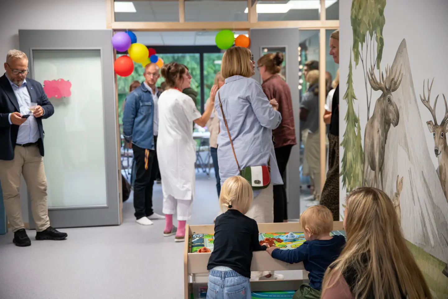 Många människor samlade i en lokal. Små barn leker med leksaker.