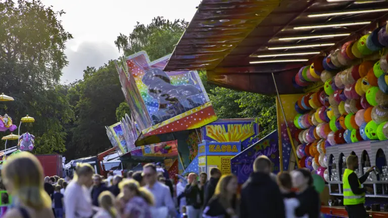 Parktorget med tivoli i vacker kvällsol, stånd med tävlingar för att vinna prylar och godis