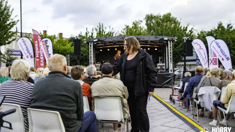En kvinna räcker mikrofonen till en person i publiken, scen i bakgrunden
