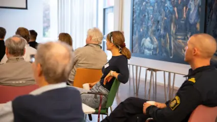 Människor som sitter ipå stolar i en sal och lyssnar.