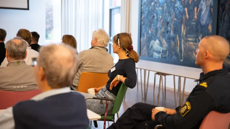 Människor som sitter ipå stolar i en sal och lyssnar.