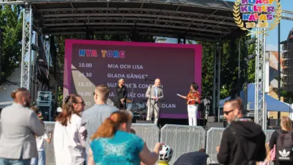 flera personer står framför en scen där tre personer pratar i mikrofoner.