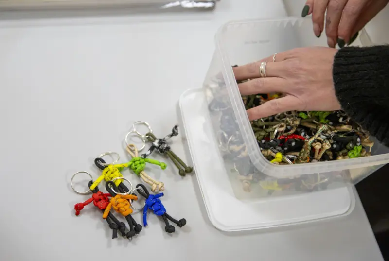 En hand gr&auml;ver i en burk med pysslade nyckelringar med p&auml;rlor i form at personer. Ett par f&auml;rgglada nyckelringar ligger bredvid l&aring;dan