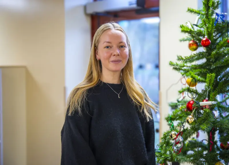 Ung kvinna i portr&auml;tt i upplyst korridor bredvid en julgran