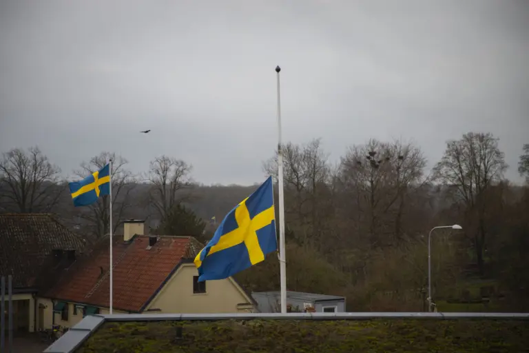 Svensk flagga vajar på halvstång i mulet väder.