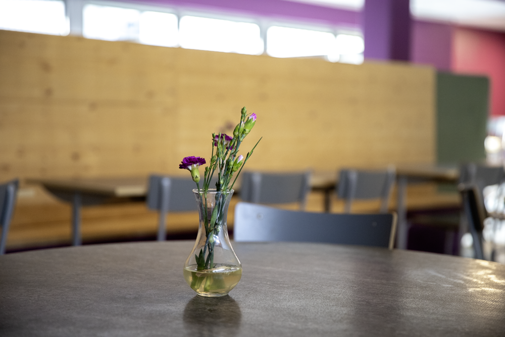 Ett litet knippe blommor i en glasvas på ett bord i skolrestaurangen.