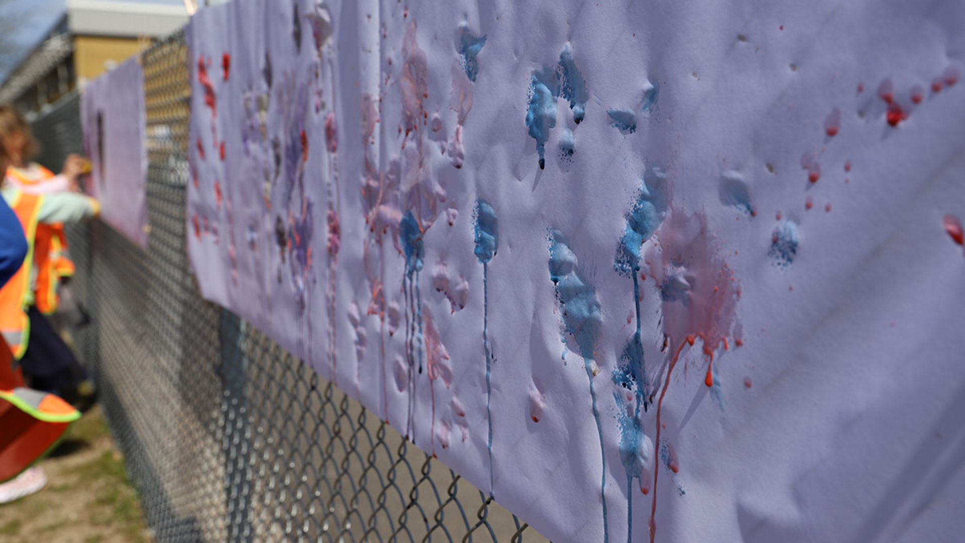 Ett stort papper upphängt på ett staket med olika färger målade på.