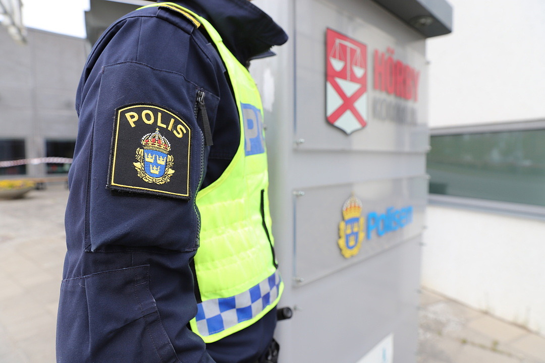 Del av polisuniform framför skylt med Hörby kommun logga och polisens logga.