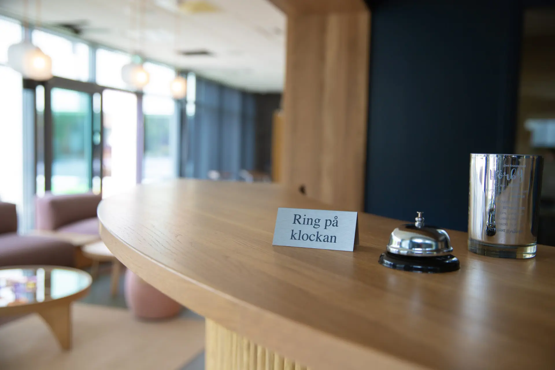 Närbild på receptionsdisk med ringklocka och skylt med texten "ring på klockan" i fokus.