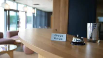 Närbild på receptionsdisk med ringklocka och skylt med texten "ring på klockan" i fokus.