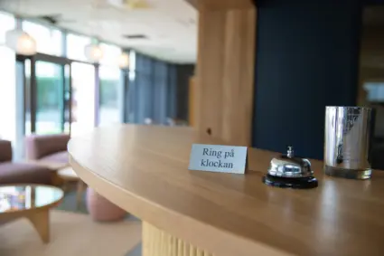 Närbild på receptionsdisk med ringklocka och skylt med texten "ring på klockan" i fokus.