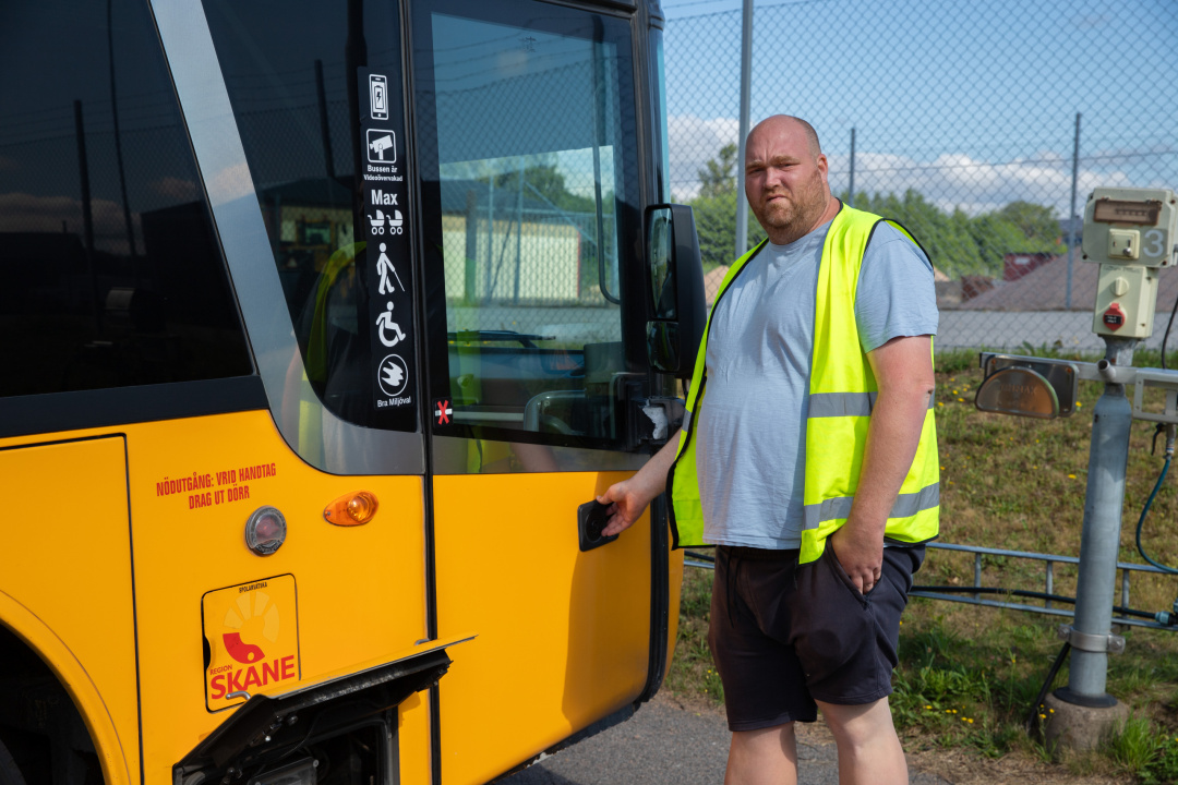 Man i gul varselväst står vid förardörren till en gul regionsbuss.